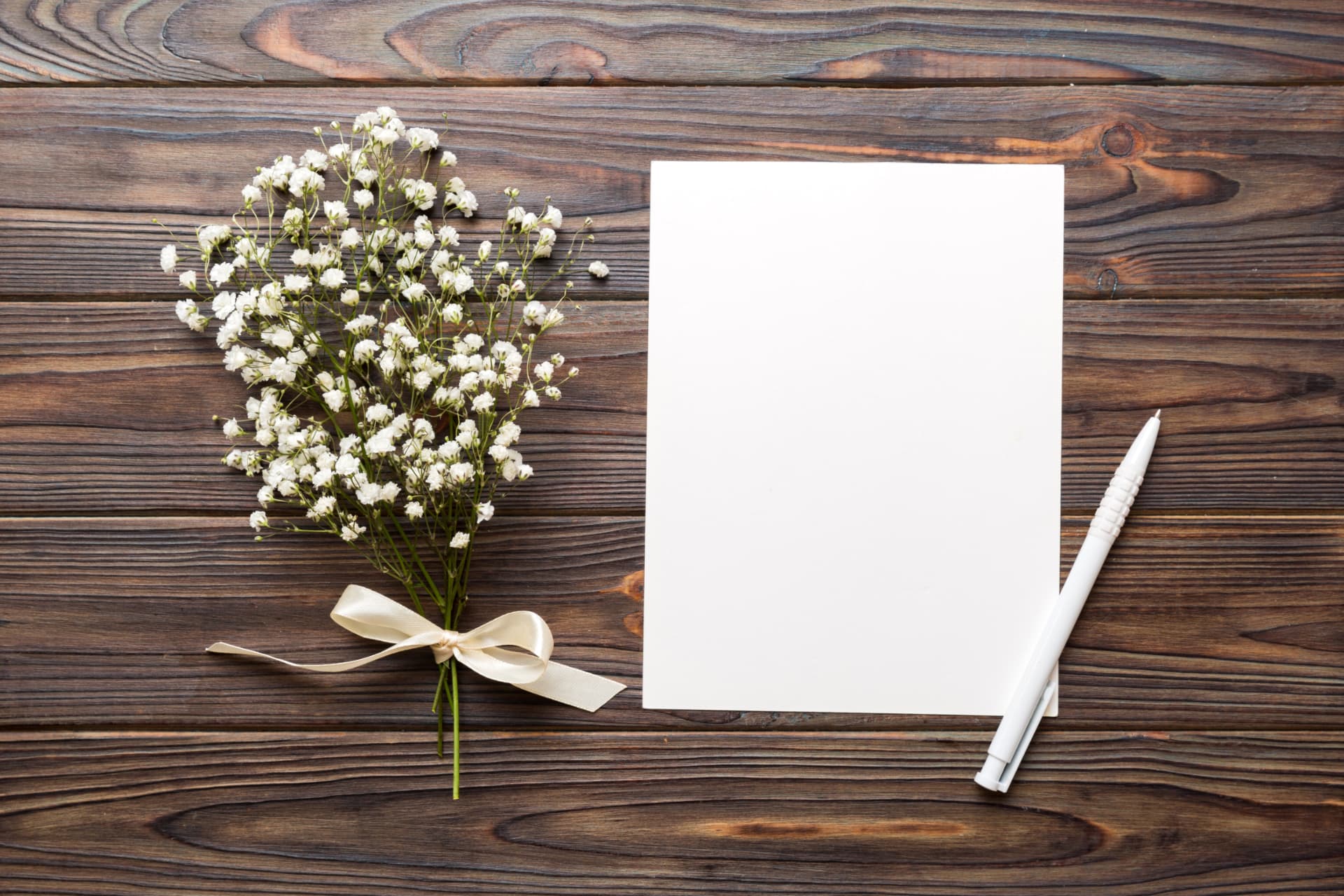 Weiße Karte mit Stift und Blumen auf Holz